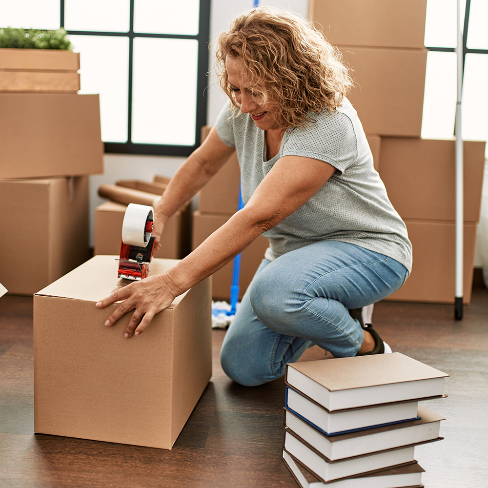 Middle age caucasian woman smiling happy packing carboard box at new home.