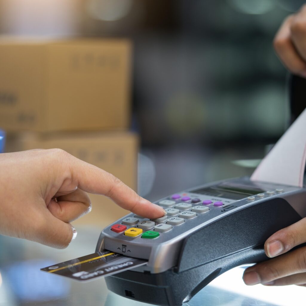 A close-up of a person entering a PIN on a payment terminal while a credit card is inserted.